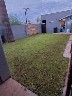 A residential backyard with a grassy lawn, a wooden fence, and a grey building with a door and windows. - Upstairs studio on 13 st (Phoenix)