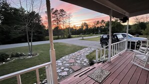 A wooden deck with a stone pathway leading to a driveway, surrounded by trees and parked vehicles. - The best of Up North! (Honor)
