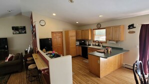 A modern kitchen with wooden cabinets, a built-in island, and a dining area with bar stools. - The best of Up North! (Honor)