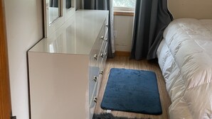 A bedroom with a white dresser, a bed with white bedding, a blue rug, and grey curtains. - The best of Up North! (Honor)