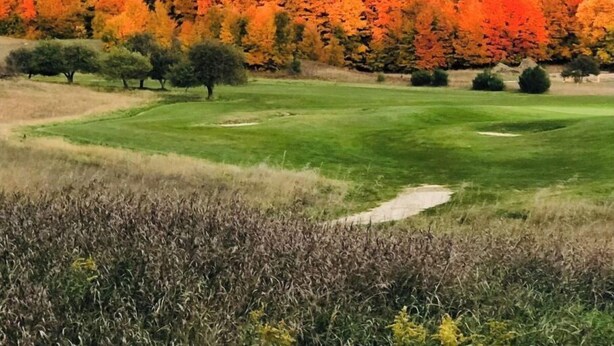 A golf course with a well-maintained green, sand bunkers, and a backdrop of autumn-colored trees. - The best of Up North! (Honor)