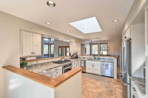 A modern kitchen with white cabinets, granite countertops, a skylight, and stainless steel appliances.