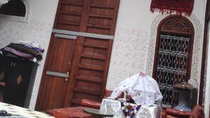 Une pièce avec une porte en bois, une petite table recouverte d’une nappe blanche, un canapé rouge et un mur orné de motifs.