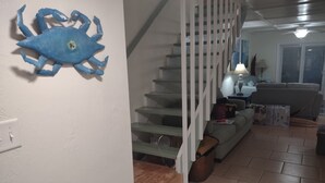 Una scala con ringhiere bianche conduce a un secondo piano. Sulla parete, una decorazione a forma di granchio blu. Un divano e una lampada si trovano al piano inferiore.