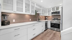 Una cocina moderna con armarios blancos, horno de acero inoxidable, microondas y licuadora.