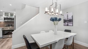 Una cocina moderna con electrodomésticos de acero inoxidable, una mesa de comedor blanca con cuatro sillas y una araña.