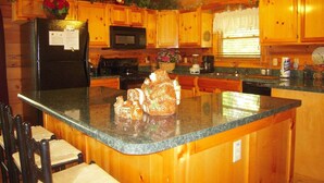 A kitchen with wooden cabinets, a granite countertop, a refrigerator, a microwave, and a sink. - Amazing Grace in Shagbark (Pigeon Forge)