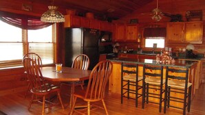 A wooden interior with a dining table and chairs, a kitchen area with a refrigerator and microwave, and a bar counter with stools. - Amazing Grace in Shagbark (Pigeon Forge)