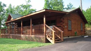 A wooden cabin with a porch, a staircase leading to the entrance, and a paved driveway. - Amazing Grace in Shagbark (Pigeon Forge)