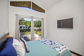 A bedroom with a bed, a TV mounted on the wall, and a balcony with a view of greenery.