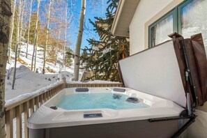 A hot tub with a control panel, set against a snowy landscape with trees and a building in the background. - Modern Home by InvitedHome | Ski In/Out, Near BC Village, Deck, Hot Tub (Avon)