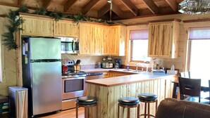 Una cocina con gabinetes de madera, un refrigerador de acero inoxidable, un horno, un microondas, un lavamanos y una zona de bar con taburetes.