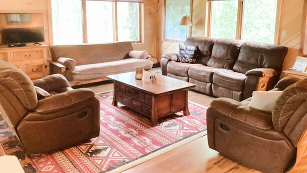 Un salón acogedor con techo de madera, un sofá de cuero marrón, un sofá blanco y una mesa de centro.