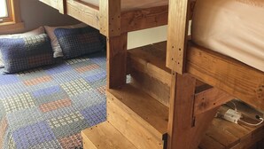 Una cama nido de madera con un estante inferior, una manta estampada y una ventana con persianas.