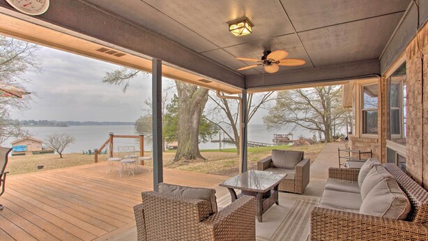 A covered outdoor deck with wicker furniture, a ceiling fan, and a view of a lake. - Roomy Texas Lake Retreat w/ Private Boat Ramp (Frankston)