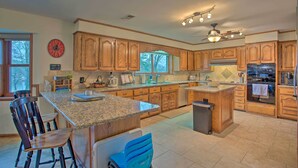 A spacious kitchen with wooden cabinets, granite countertops, a central island, bar stools, and a ceiling fan. - Roomy Texas Lake Retreat w/ Private Boat Ramp (Frankston)