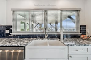 A kitchen with a double sink, stainless steel dishwasher, and a window with blinds.