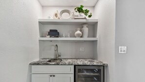 Een kleine keuken met witte kastjes, een granieten aanrechtblad, een inbouwoven en een plank met decoratieve objecten.