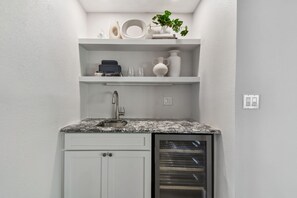 Una cocina compacta con armarios blancos, encimera de granito, horno empotrado y repisa con adornos.