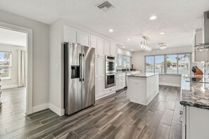 A modern kitchen with stainless steel appliances, white cabinetry, and a large island with a marble countertop. - Waterfront Home with Heated Pool! 2 miles from Beach! (St. Petersburg)