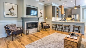 A modern living room with a fireplace, a television, and a kitchen area with bar stools. - Sunny FL Home 'Miss Millie’s Landing’' w/ Deck! (Santa Rosa Beach)