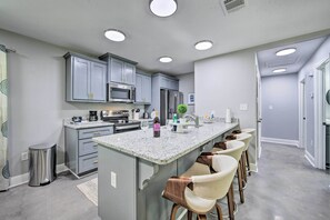A modern kitchen with grey cabinets, a central island with bar stools, stainless steel appliances, and recessed ceiling lights. - Modern Lakefront Retreat in Avinger (Avinger)
