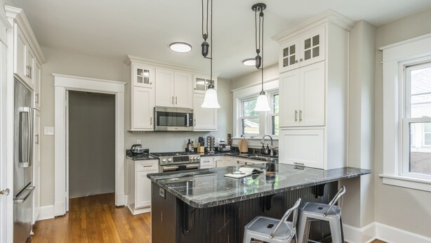A modern kitchen with white cabinets, a large island with bar stools, stainless steel appliances, and pendant lighting. - Stylish 2Bed/2Ba home in Chevy Chase, close to Downtown and UK! (Lexington)