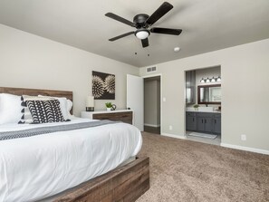 Relax in this serene bedroom with a large bed and ceiling fan, featuring a wall-mounted artwork and adjacent bathroom.