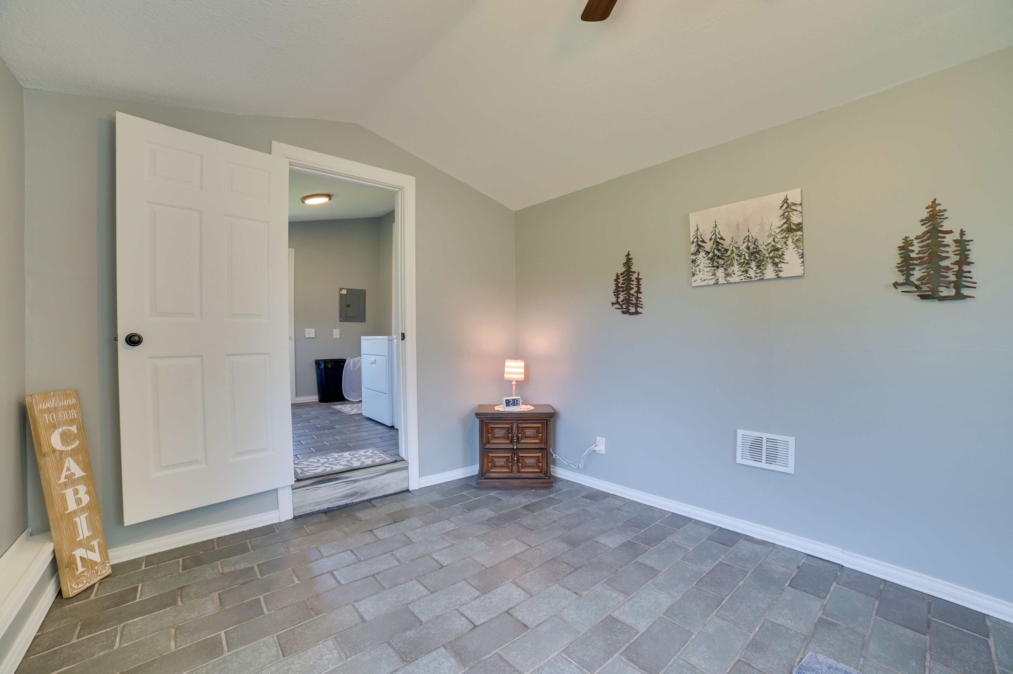 A hallway with a wooden door, a welcome sign, a nightstand with a lamp, and wall decorations.