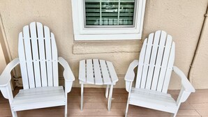 Two white Adirondack chairs and a small table on a wooden deck.