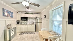 A kitchen with white cabinets, a stainless steel refrigerator, a microwave, and a ceiling fan.