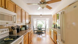 Une cuisine dotée de meubles en bois, d’une cuisinière, d’un four à micro-ondes, d’un ventilateur de plafond et d’un coin repas avec une table et des chaises.