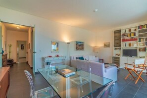 A modern living room with a glass dining table, a sofa, and a bookshelf. - SUPER ATTICO - Sea view and large terrace (Rapallo)