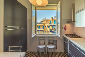 Une cuisine avec une fenêtre, deux chaises, une table et un fourneau.