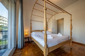 Un lit à baldaquin dans une pièce dotée d’une grande fenêtre, d’une table de chevet et d’une porte.