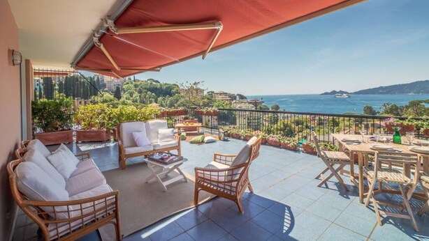 A balcony with wicker furniture, a table set for dining, and a view of the sea and hills. - SUPER ATTICO - Sea view and large terrace (Rapallo)