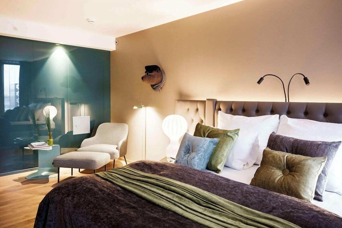 Un dormitorio moderno con una cama grande, una zona de estar y vistas a la ciudad.
