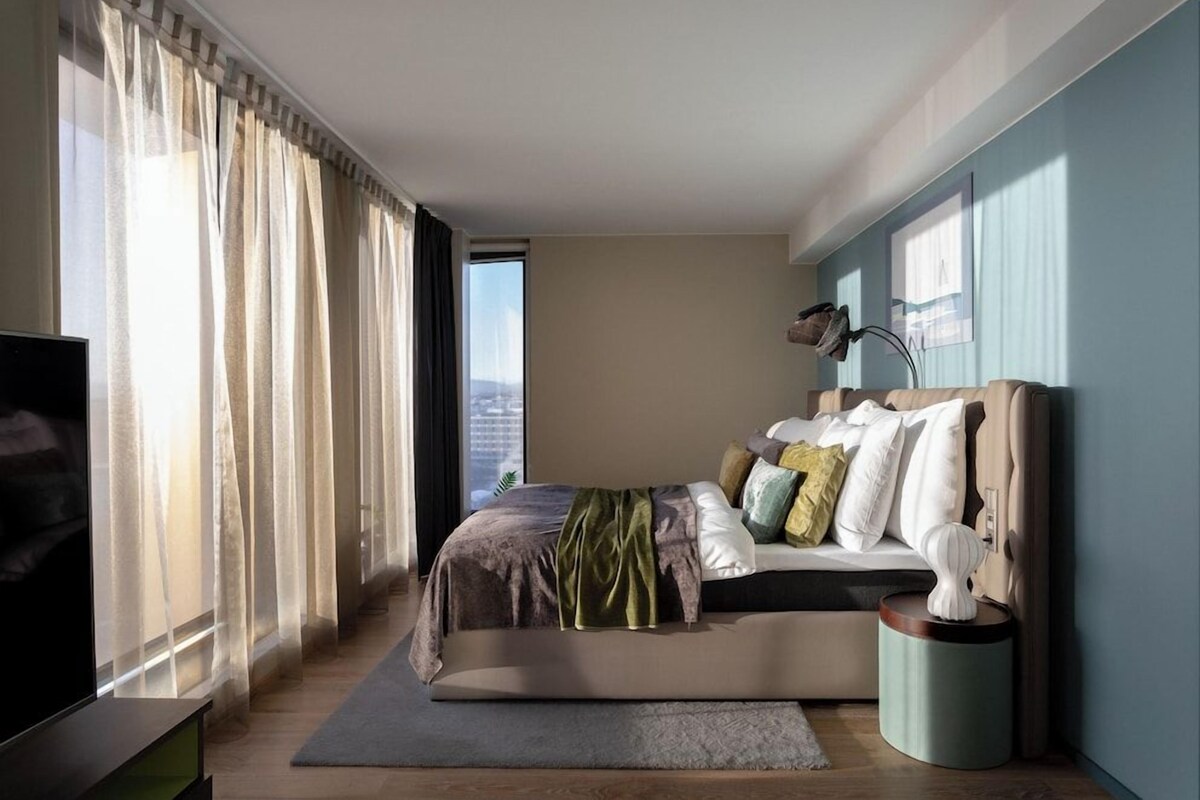 Un dormitorio moderno con una cama, una mesita auxiliar, una lámpara y un televisor.
