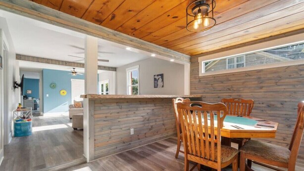 Un comedor con mesa y sillas de madera, una cocina al fondo y vista al exterior.