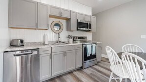 Una cocina moderna con electrodomésticos de acero inoxidable, armarios blancos y un comedor con sillas blancas.