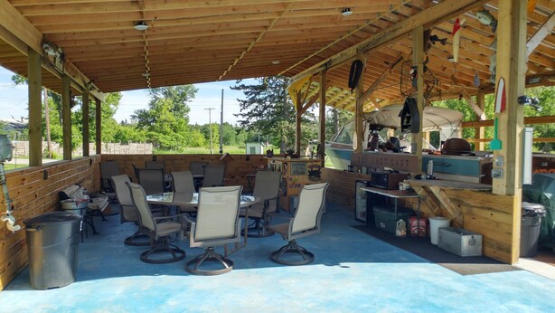 An outdoor patio with wooden tables and chairs, a barbecue grill, and a welcome sign.