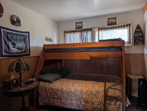 A bunk bed room with a floral bedspread, a small table with a lamp, and wall decorations including a fish and mountain scene.