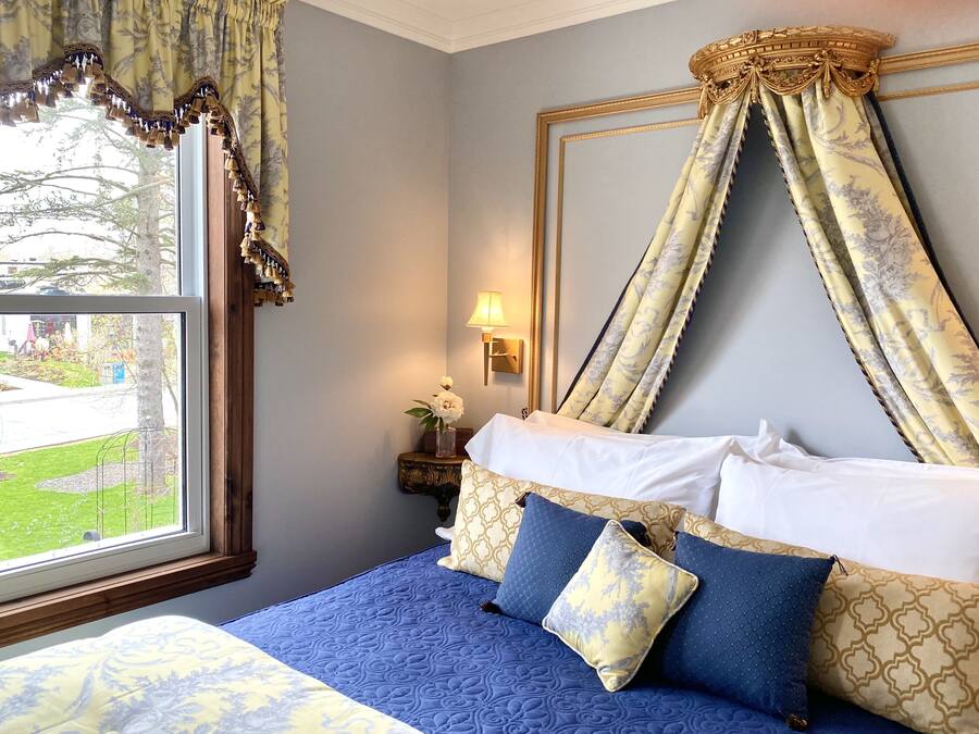 Una camera da letto con un letto a baldacchino, vista sul giardino attraverso la finestra e un comodino con una lampada.