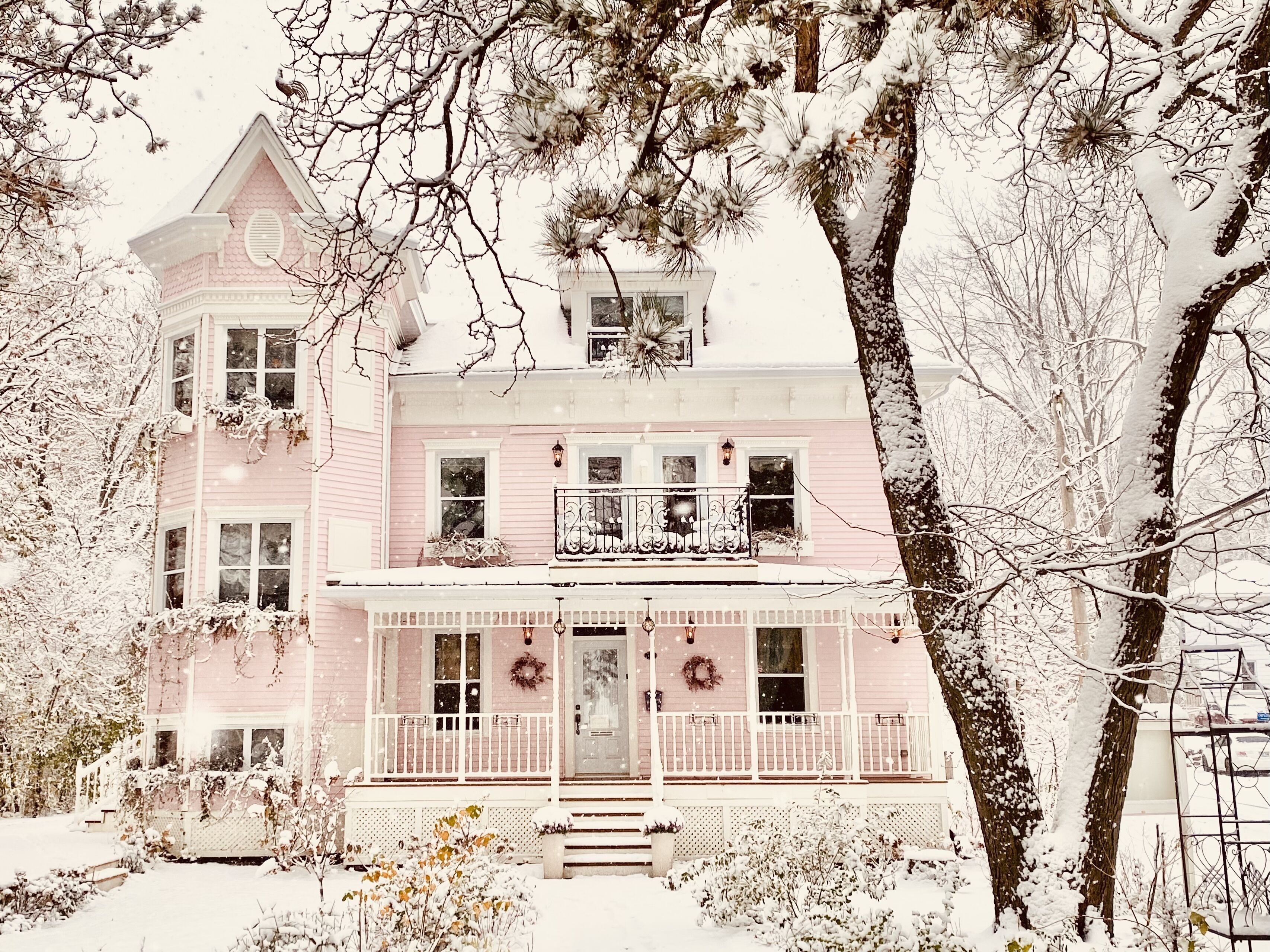 Een roze huis met twee verdiepingen, een veranda, een voordeur en een klein balkon.
