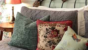 A bedroom with a bed, floral wallpaper, and a decorative headboard.
