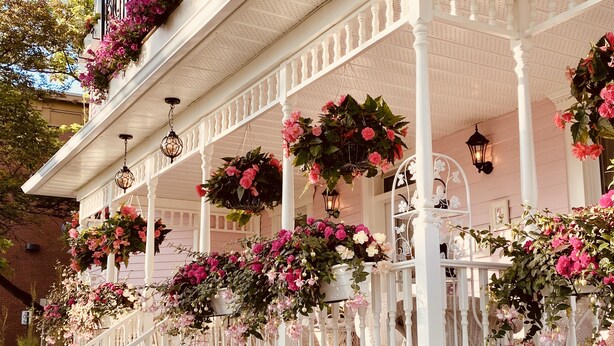 A white porch with multiple hanging flower baskets and white railings. - Maison Rose (Hudson)
