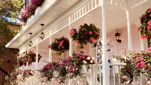 A white porch with multiple hanging flower baskets and white railings. - Maison Rose (Hudson)
