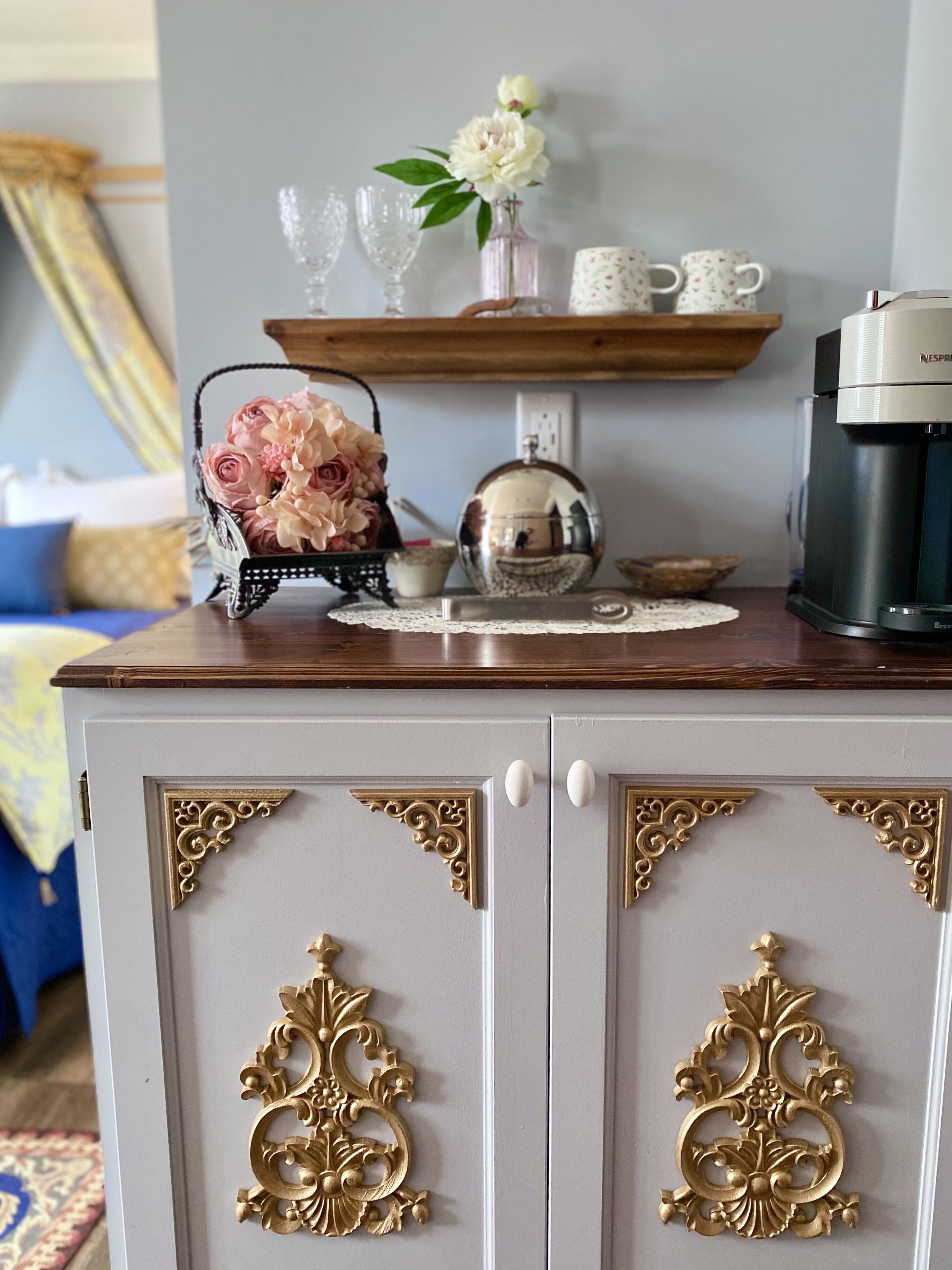 Zona cuina amb cafetera, un vas amb flors i un mirall decoratiu.