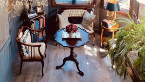 A room with a chandelier, bookshelves, a sofa, a table with a vase, and a window with curtains. - Maison Rose (Hudson)