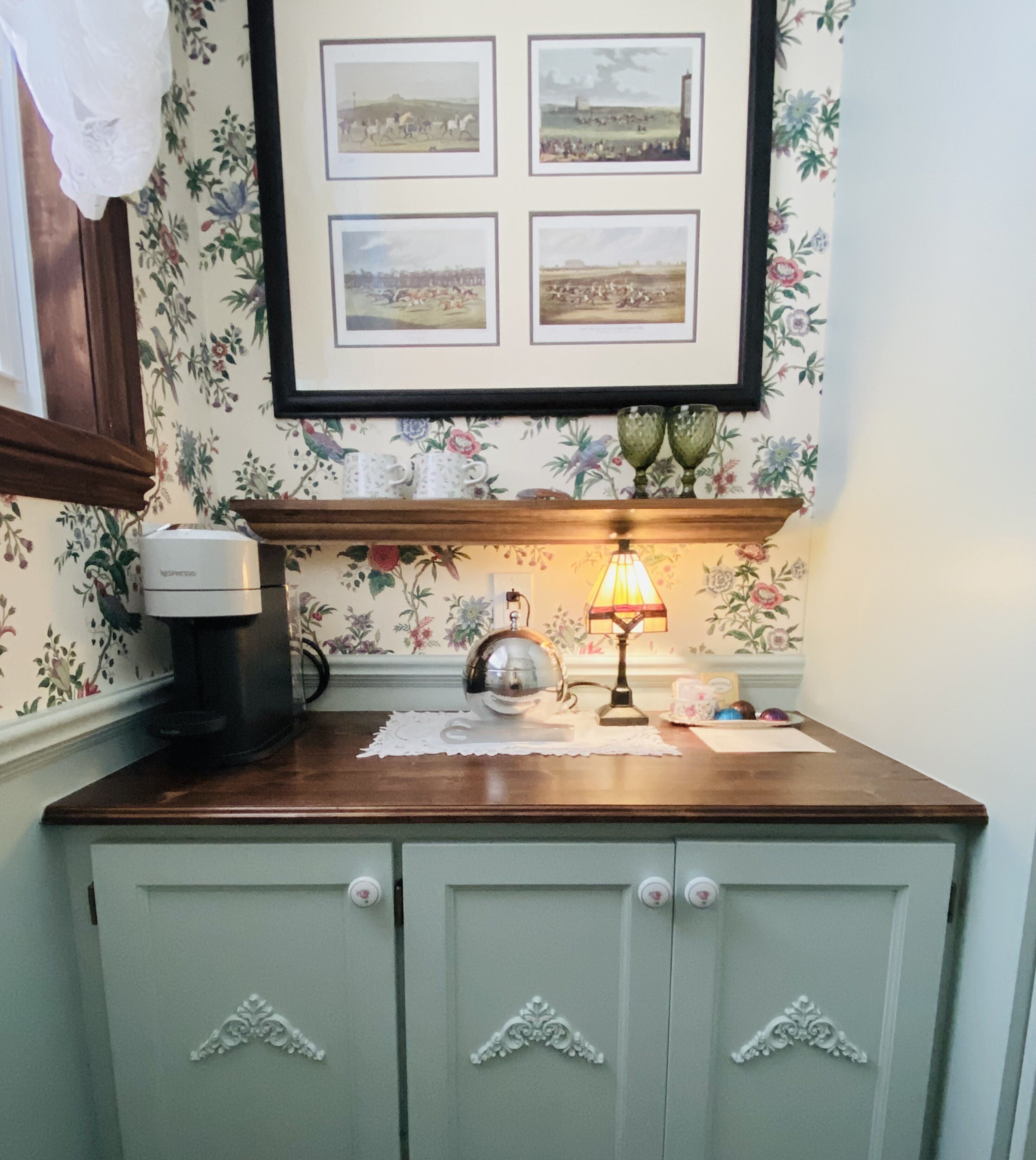 A kitchen with a coffee maker, a lamp, and framed pictures on the wall.